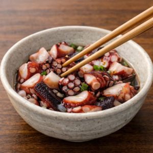 器に入れたタコのぶつ切りを菜箸でやさしくかき混ぜ、調味料をなじませている様子。